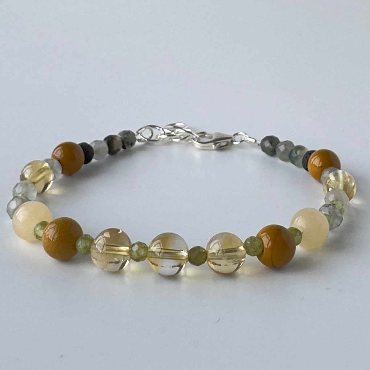 A beaded bracelet featuring a mix of brown, cream, clear, and grey faceted beads with a silver clasp, displayed on a light grey background.