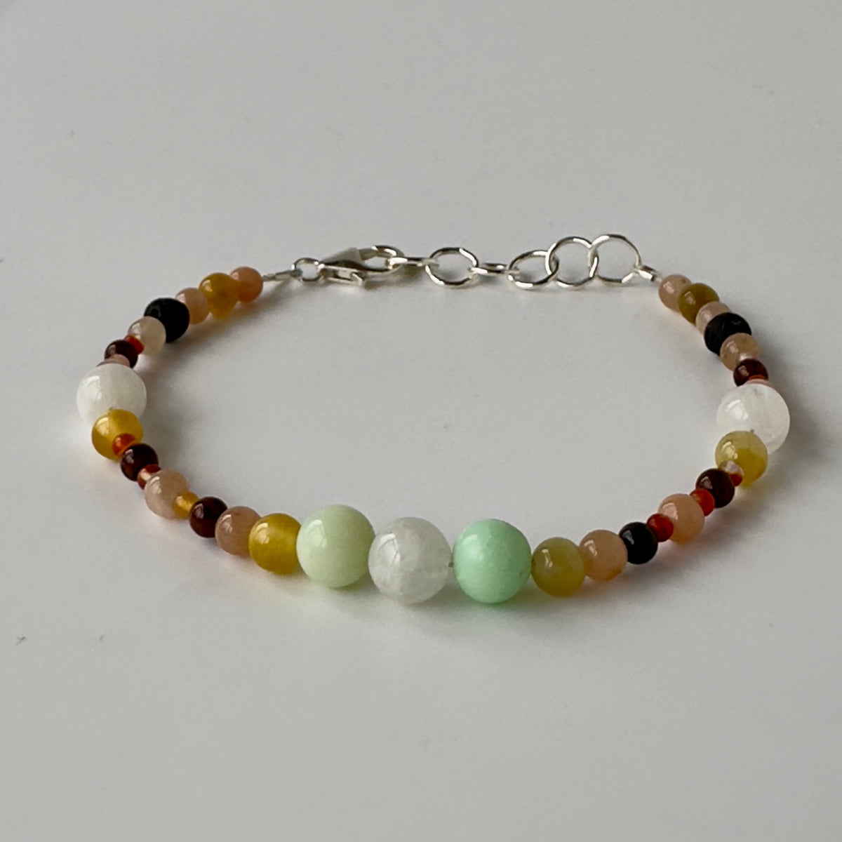 A beaded bracelet with a mix of polished round beads in white, pale green, yellow, brown, and dark red, featuring a silver lobster clasp and three circular links.