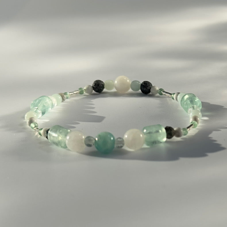 Beaded bracelet in shade of green white and grey on a pale grey background