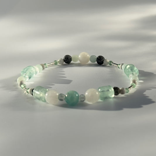 Beaded bracelet in shade of green white and grey on a pale grey background