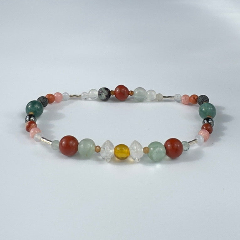 Beaded bracelet in tones of green red and pink on a pale grey background