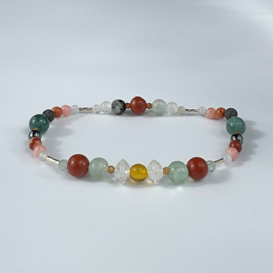 Beaded bracelet in tones of green red and pink on a pale grey background