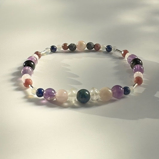 Beaded bracelet in shades of purple grey and white on a pale grey background 