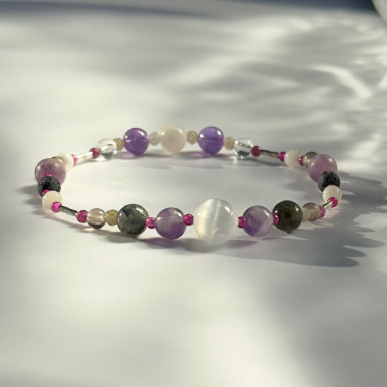 Beaded bracelet in shades of purple grey and white on a pale grey background