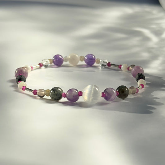 Beaded bracelet in shades of purple grey and white on a pale grey background