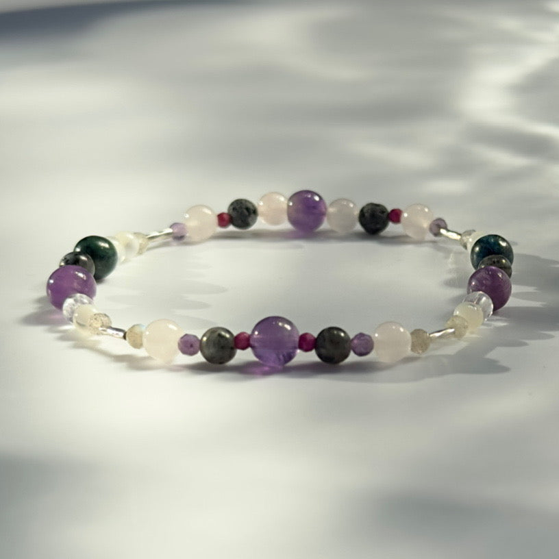 Beaded bracelet in shade of purple grey and white on a pale grey background 