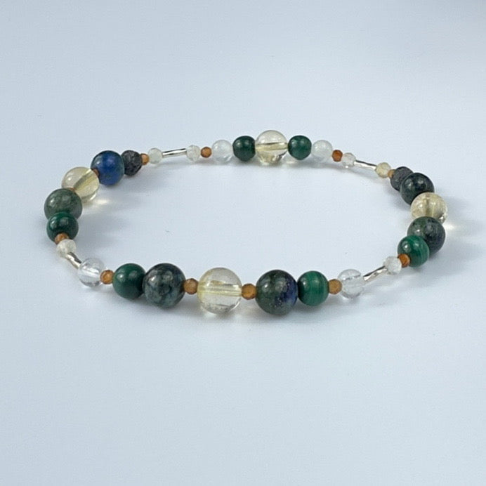 Beaded bracelet in tones of green yellow and brown on a pale grey background