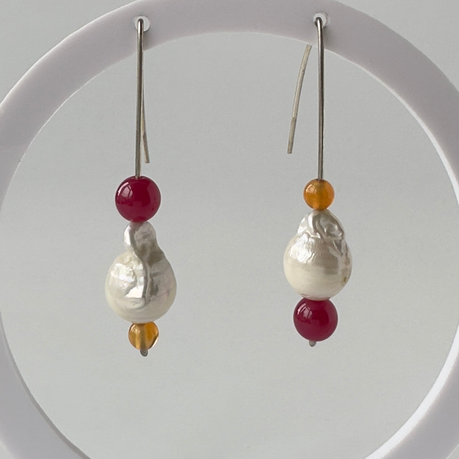 Pair of earrings with pearls and red and orange beads on a white background