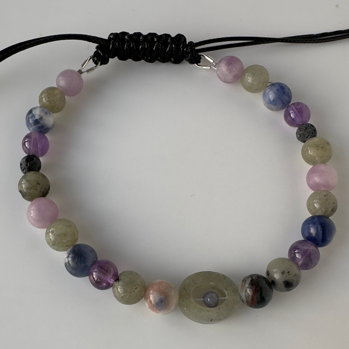 A beaded cord bracelet featuring polished round gemstone beads in shades of purple, blue, green, and pink, with a black knotted cord closure at the top.