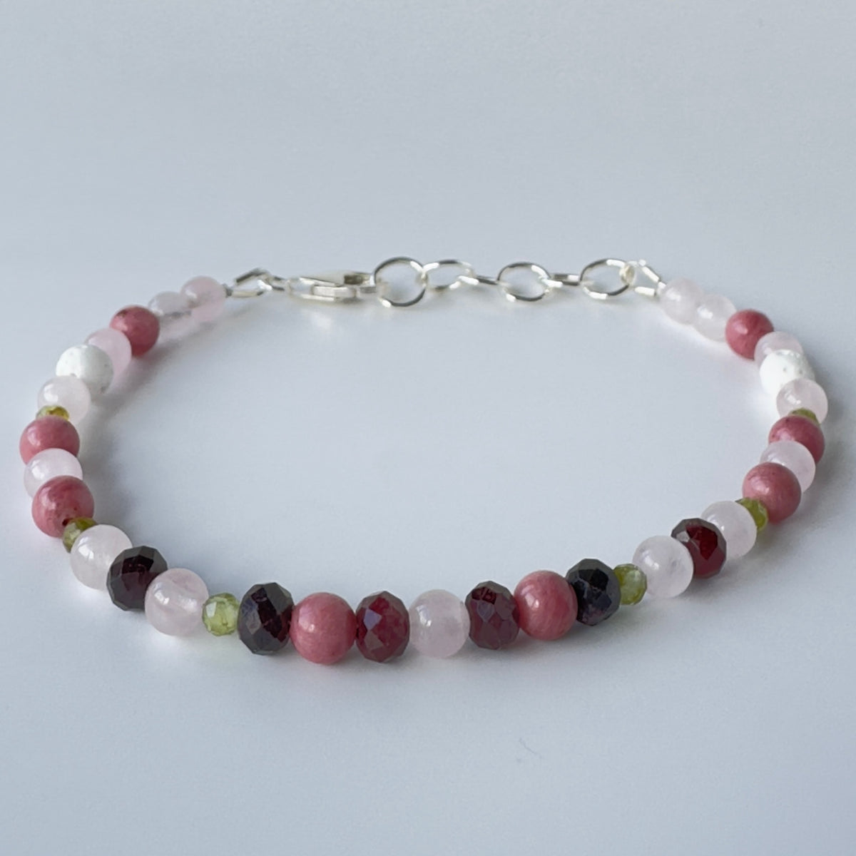 multicoloured beaded bracelet in shades of pink, red, white and green with a silver chain fastening on a pale grey background.