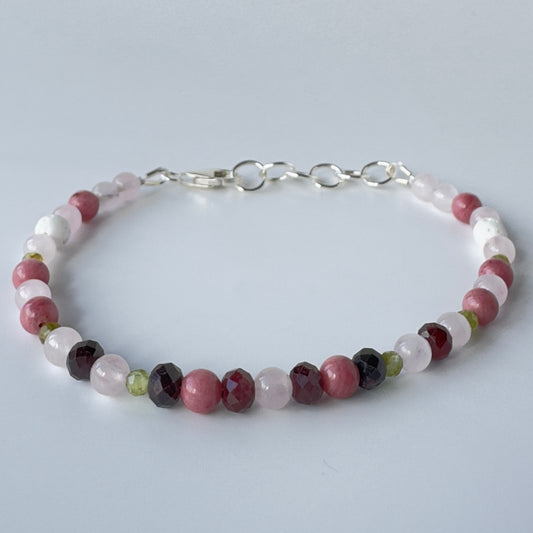 multicoloured beaded bracelet in shades of pink, red, white and green with a silver chain fastening on a pale grey background.