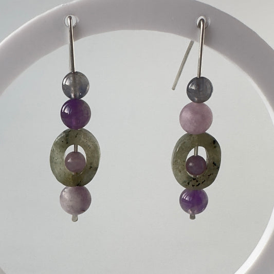 A pair of handmade drop earrings featuring labradorite ring beads, purple amethyst beads, and silver metal hooks, displayed against a white circular background.
