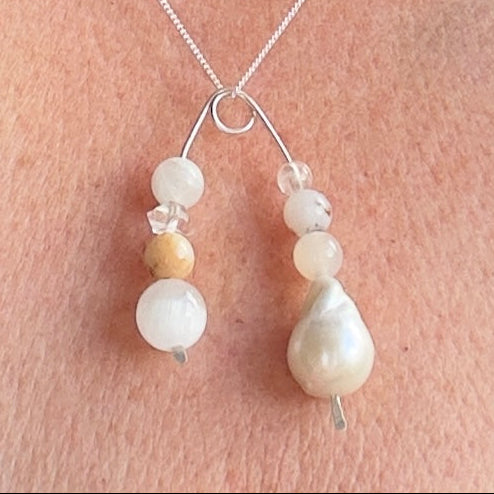 A close-up of a delicate silver necklace worn on a person's neck, featuring  a baroque pearl and white and cream beads on a fine chain.
