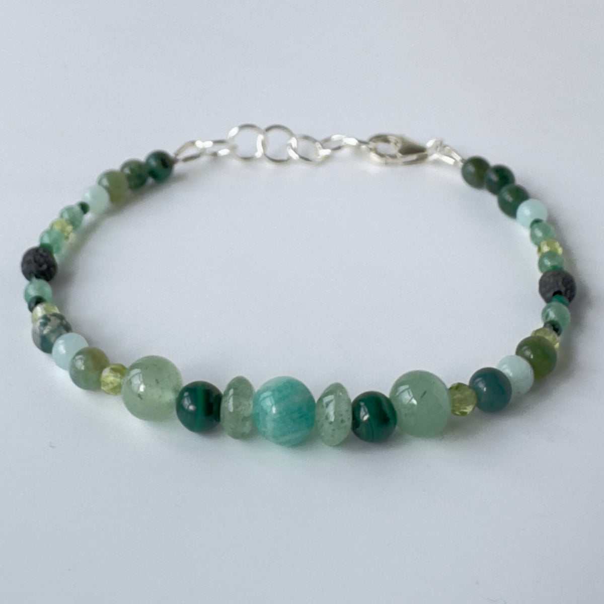 Beaded bracelet with green and sterling silver clasp on a light gray background