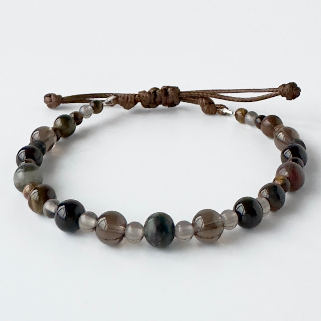 Beaded bracelet in brown and grey tones on a brown cord on a white background