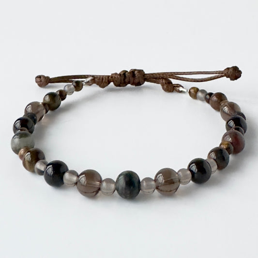 Beaded bracelet in brown and grey tones on a brown cord on a white background