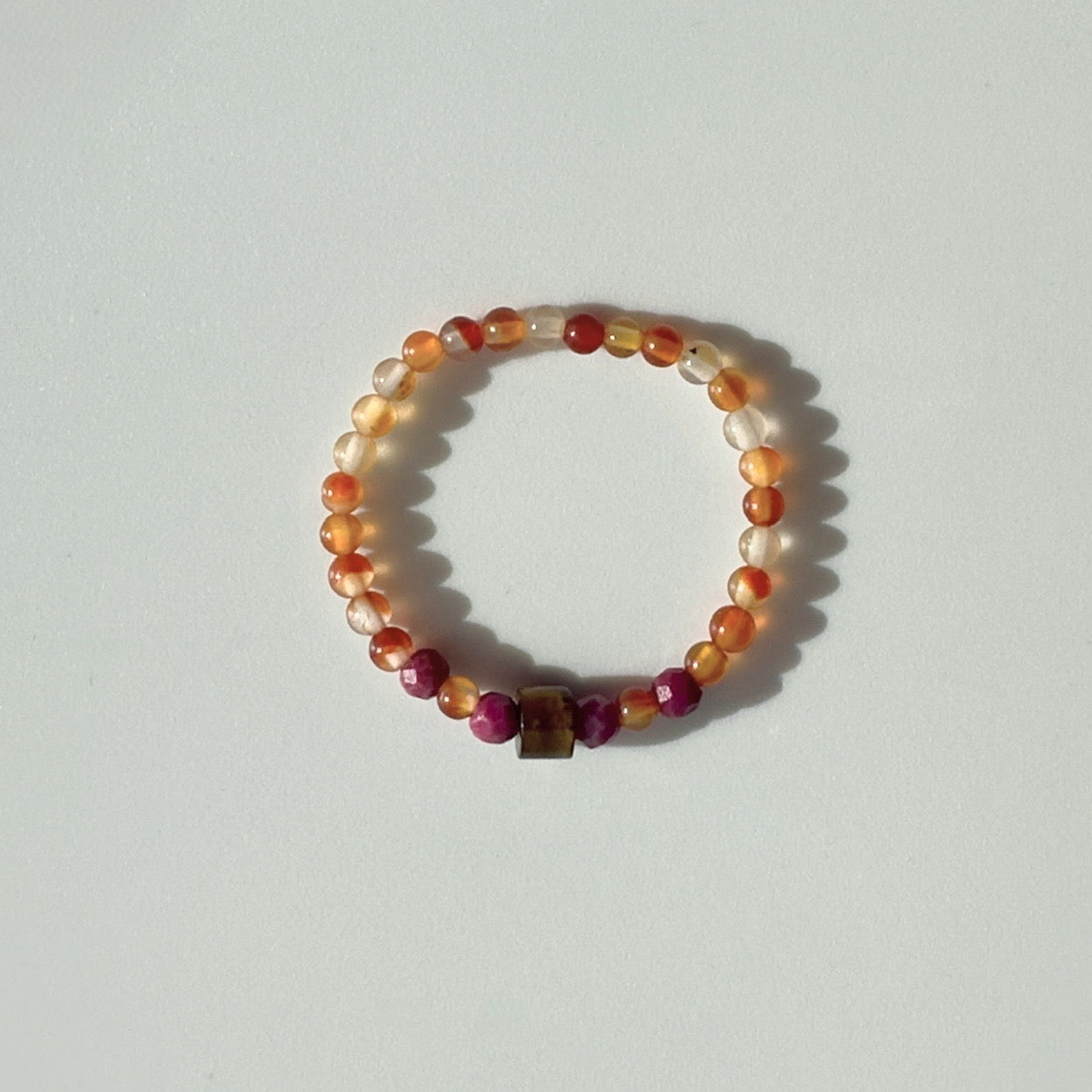 Orange and red beaded ring with central brown cylindrical bead on a pale grey background