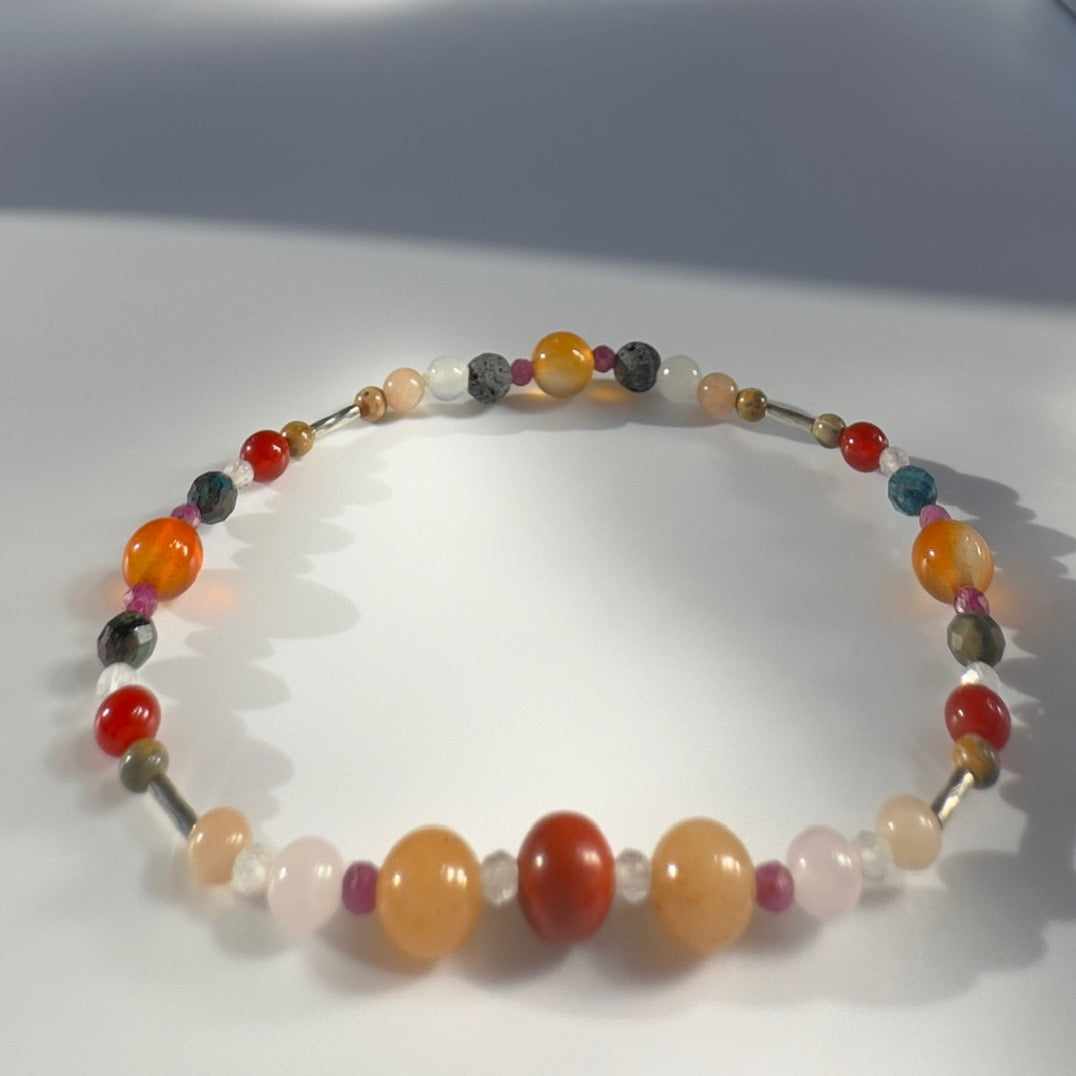 Beaded bracelet in tones of orange red and grey on a pale grey background
