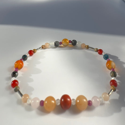Beaded bracelet in tones of orange red and grey on a pale grey background