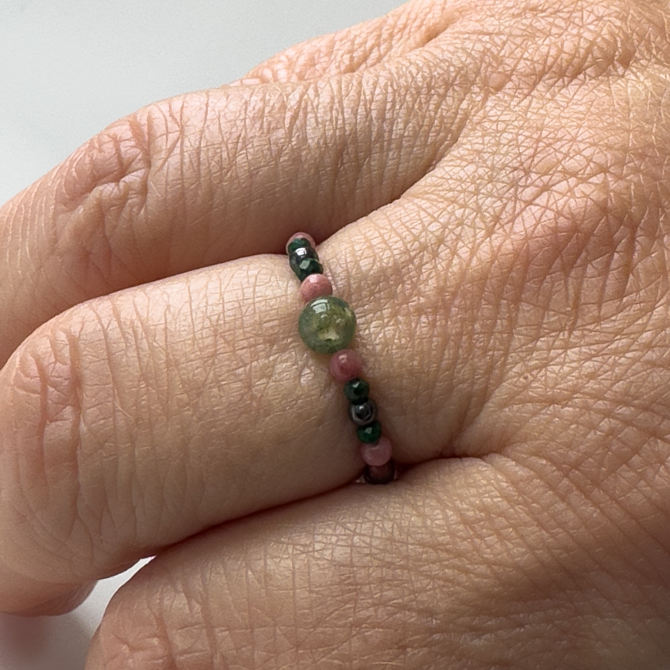 Green and pink beaded ring being worn on a finger