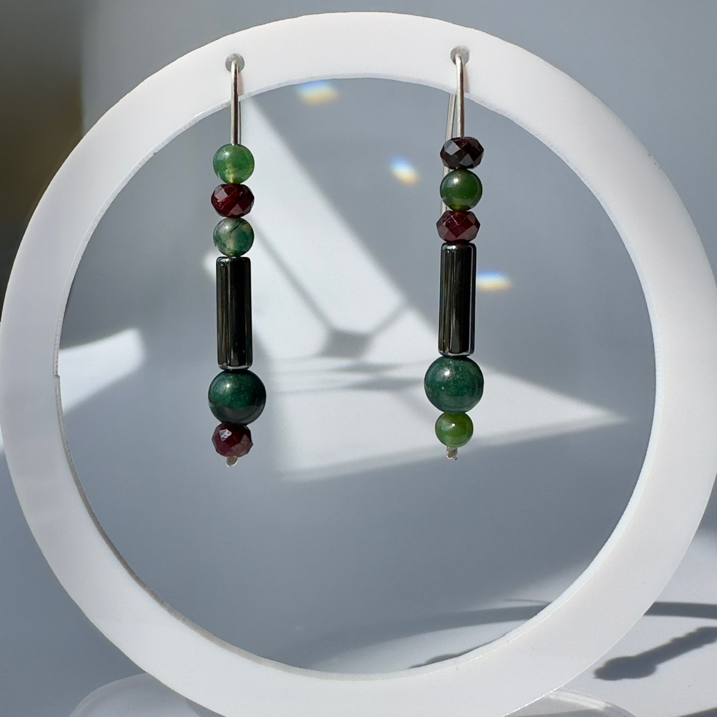 Pair of earrings with green and black beads on a white circular stand.