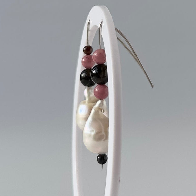 A pair of beaded and pearl drop earrings displayed on a white vertical stand against a light gray studio background.