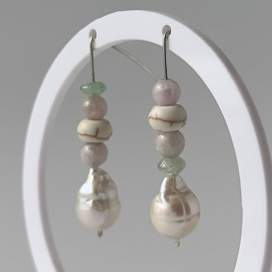 A pair of beaded pearl drop earrings displayed on a white oval stand against a light gray background.