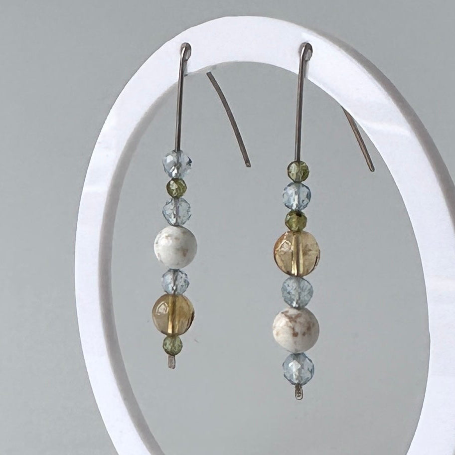 A pair of beaded dangle earrings displayed on a white circular jewelry stand against a light gray background.