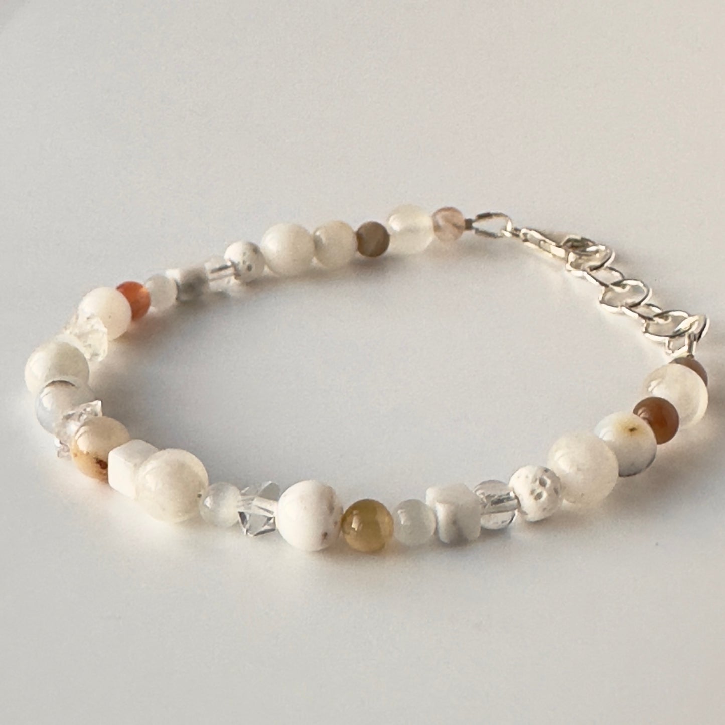 A beaded bracelet with white, cream, and brown stone beads, clear faceted crystal beads, and a silver lobster clasp, displayed on a light gray background.