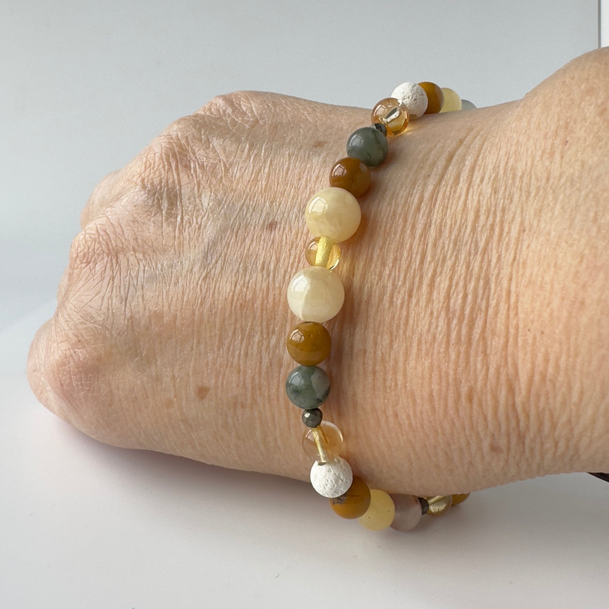 A close-up of a person's wrist wearing a beaded stretch bracelet with translucent round beads in cream, yellow, brown, and gray tones.