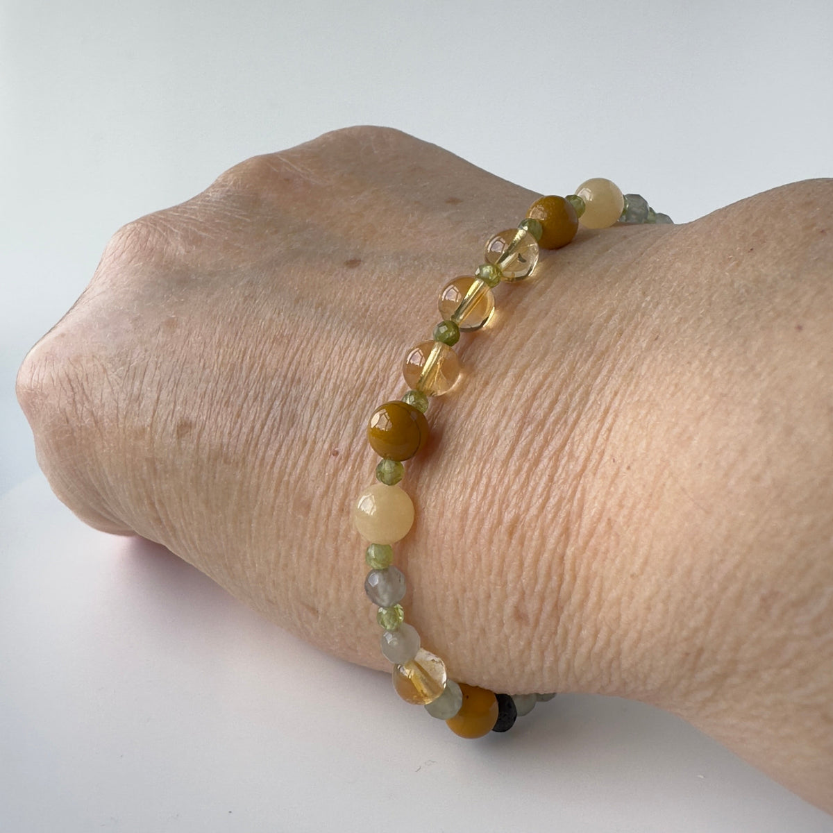 A beaded bracelet worn on a person's wrist, featuring translucent yellow and brown beads with small clear stone accents, shown against a plain white background.