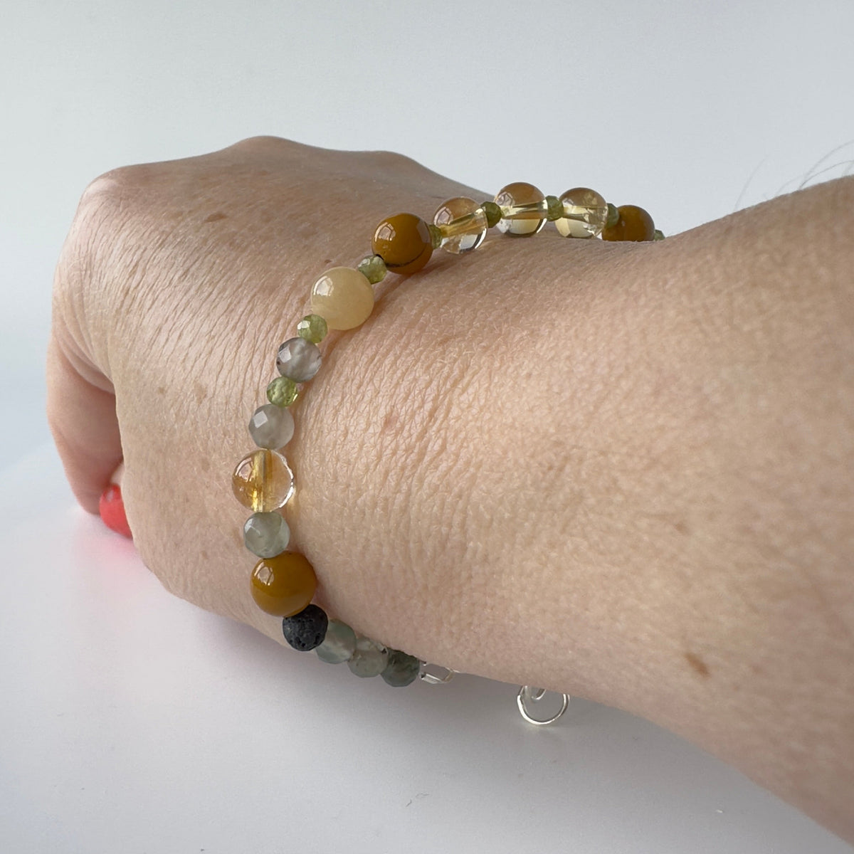 A close-up of a person's wrist wearing a beaded bracelet with translucent yellow beads and mixed beige, brown, and grey beads, shown against a plain white background.
