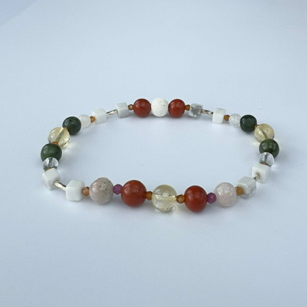 Beaded bracelet in shades of green yellow and red on a pale grey background