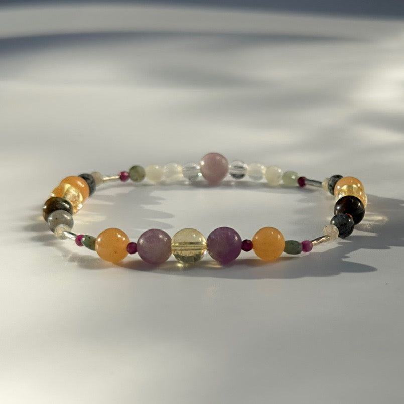 Beaded bracelet in shades of yellow purple and grey on a pale grey background