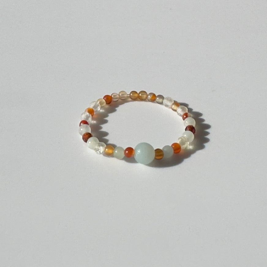 Beaded ring with white, orange, and clear beads on a light grey background