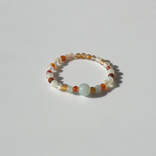 Beaded ring with white, orange, and clear beads on a light grey background