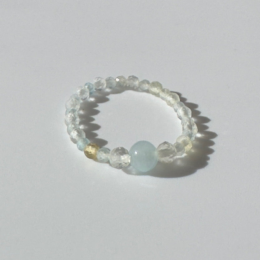 Beaded ring with a central light blue gemstone on a white background