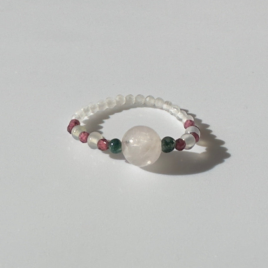 Beaded ring with a central large bead and smaller coloured beads on a light grey background