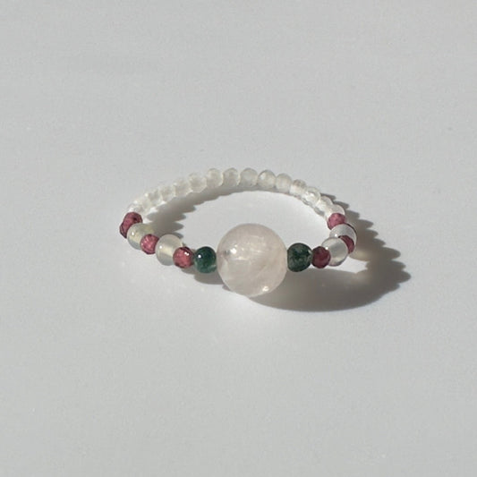 Beaded ring with a central large bead and smaller coloured beads on a light grey background