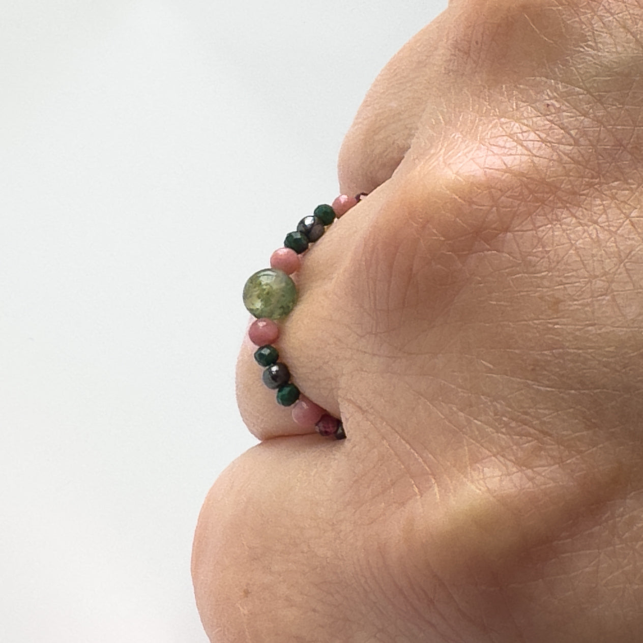 Profile view of green and pink beaded ring worn on a finger