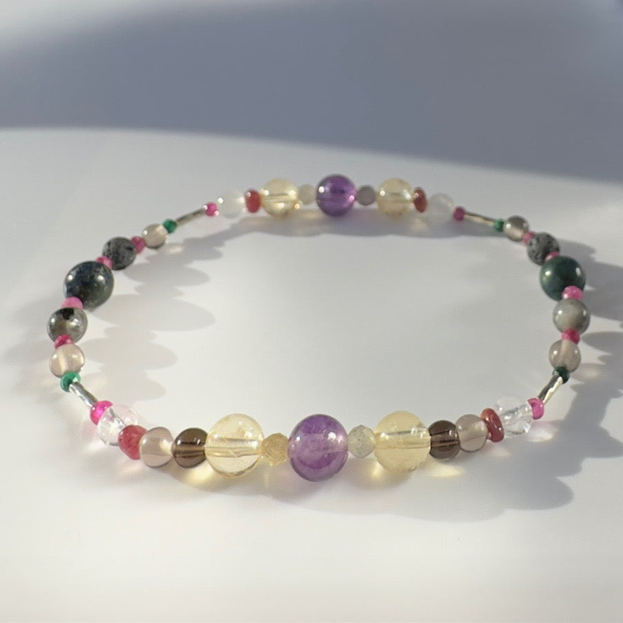 Beaded bracelet in shades of purple yellow and grey on a pale grey background