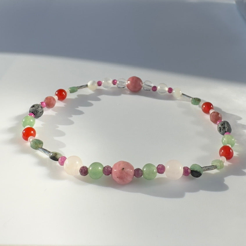 Beaded bracelet in shades of red pink and green on a pale grey background