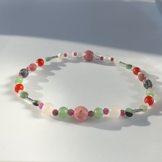Beaded bracelet in shades of red pink and green on a pale grey background