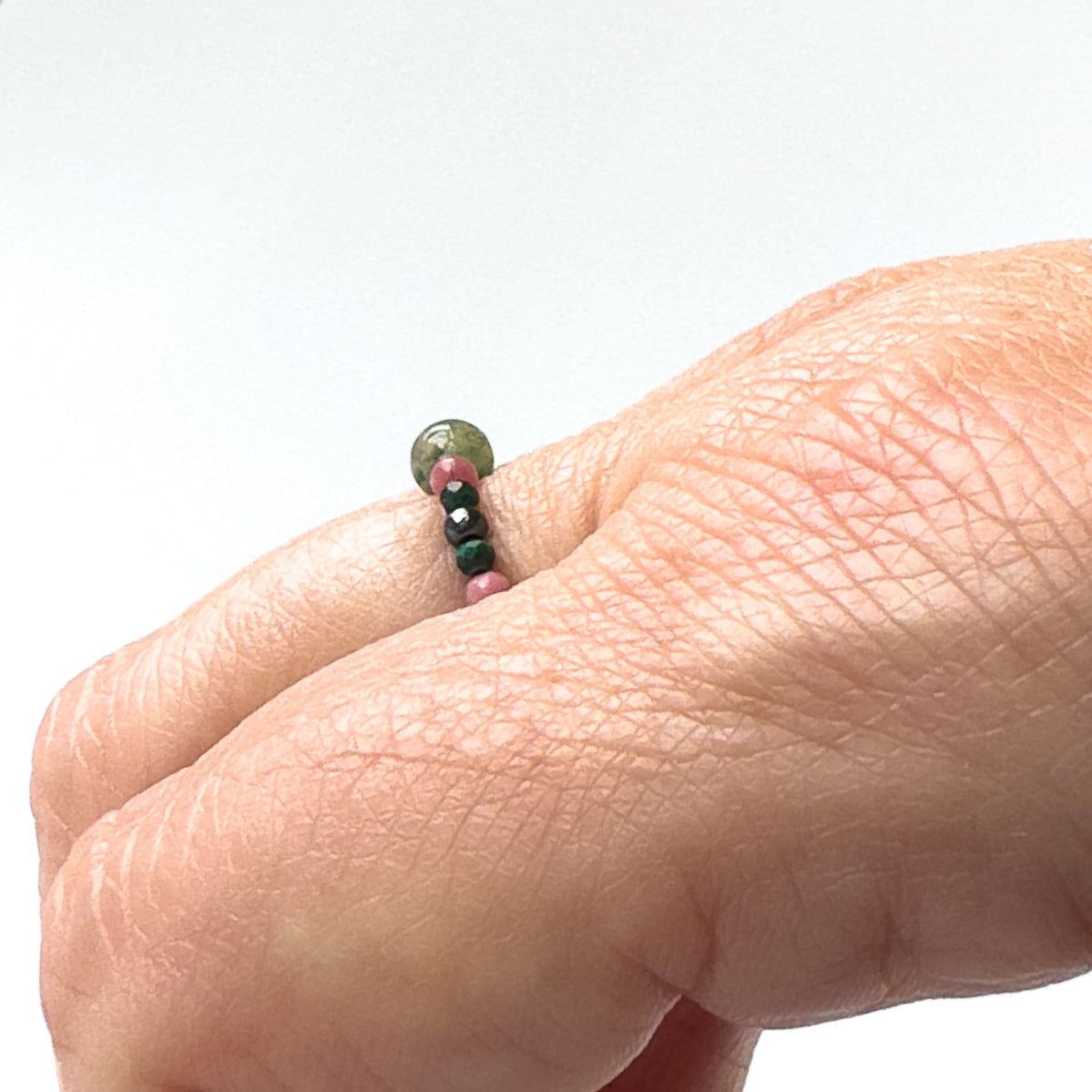 Side view of pink and green beaded ring being worn on the finger