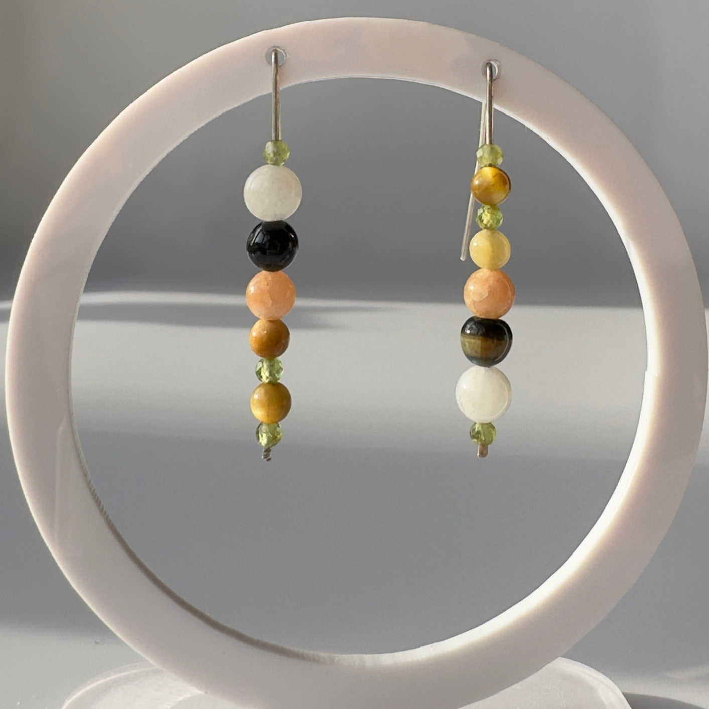 Yellow green and brown tones beaded earrings on a white circular stand with a gray background