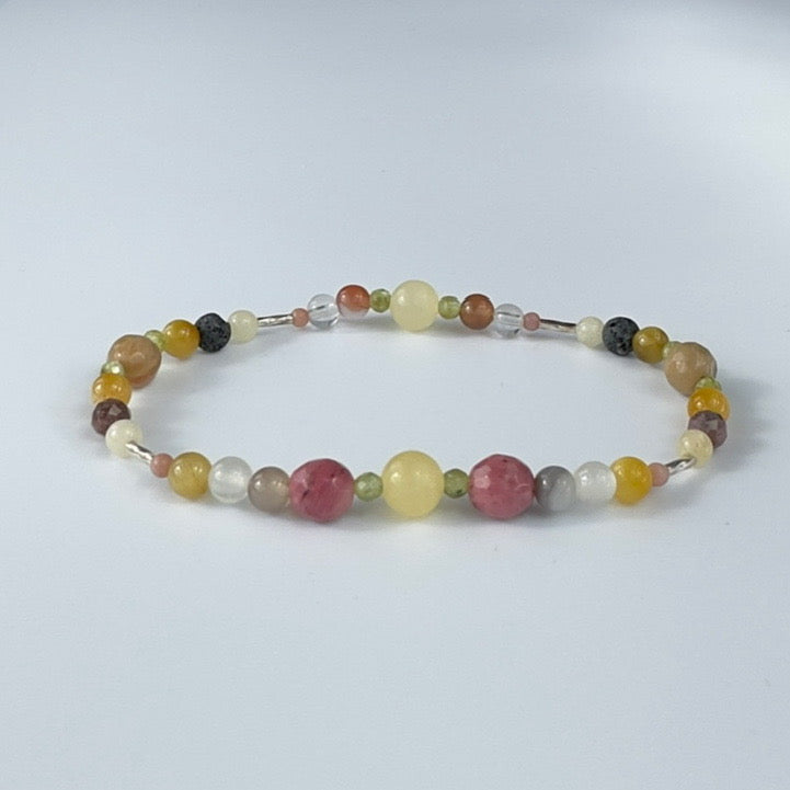 Beaded beacelet in shades of yellow brown and pink on a pale grey background